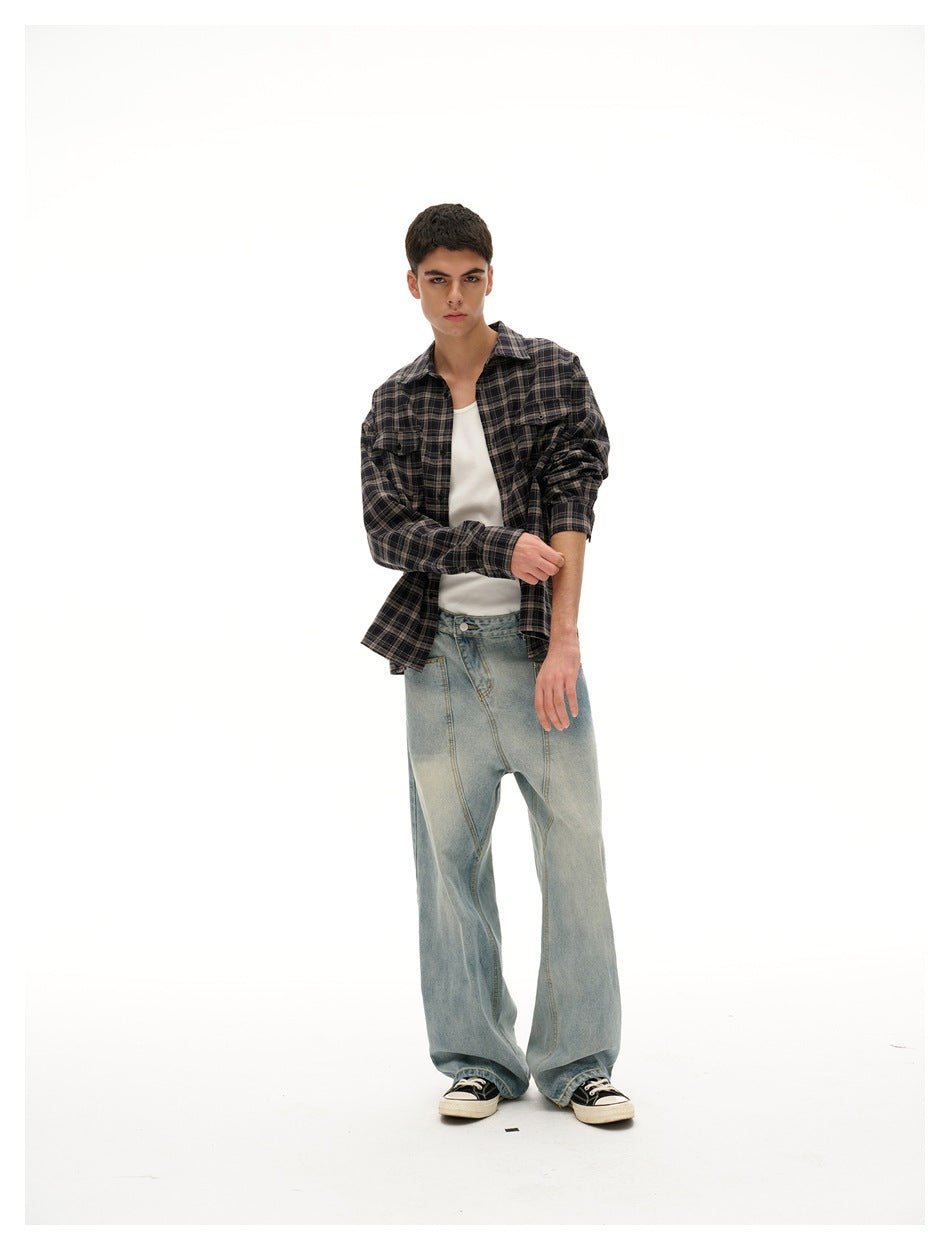 Model wearing a charcoal plaid button-up shirt over a white tee, rolling up one sleeve with loose light-wash jeans.