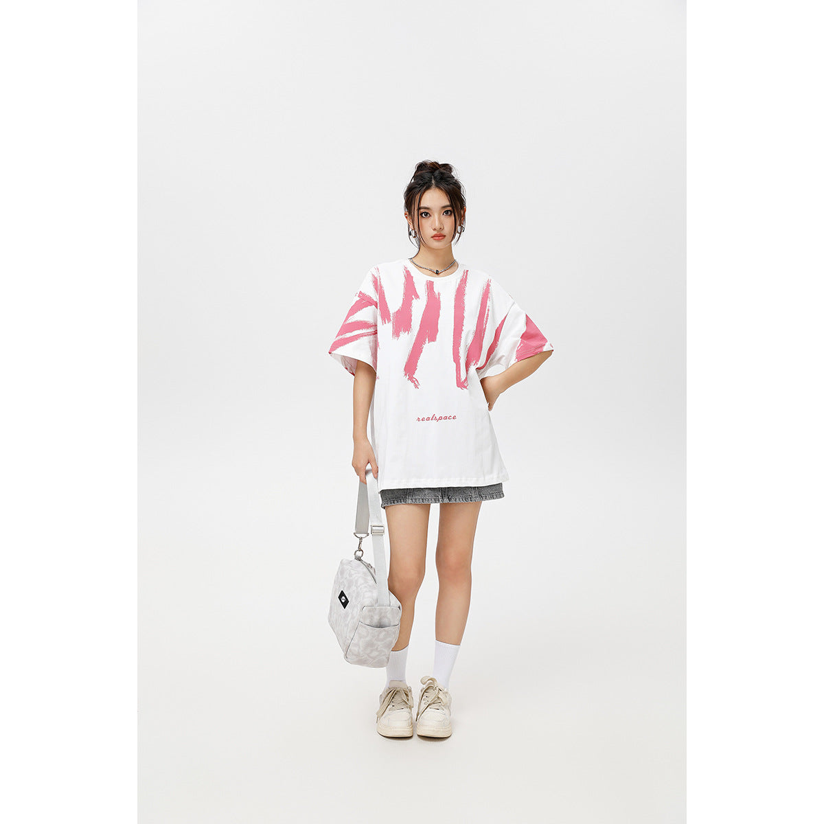 Front view of a model in an oversized white T-shirt with pink brushstroke graphics and gray shorts.