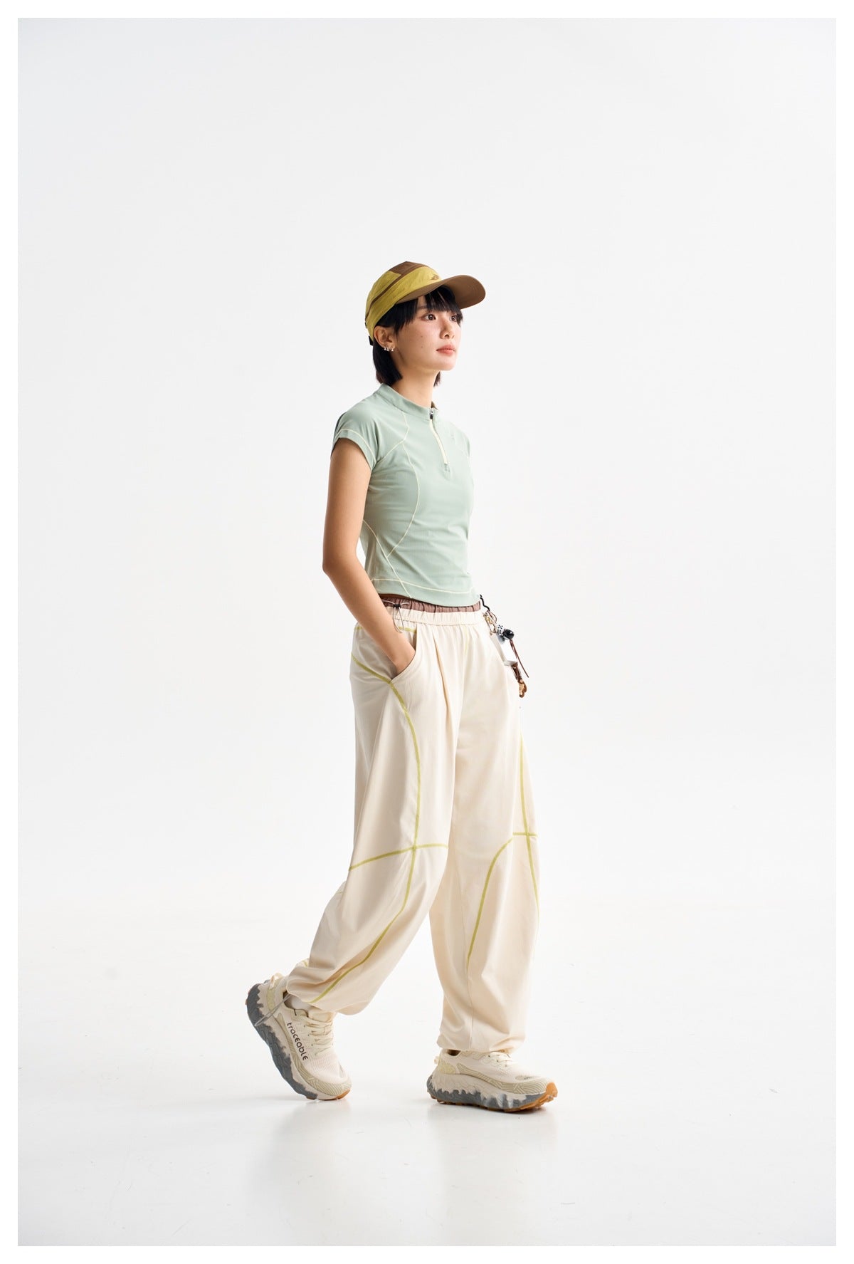 Model wearing a pale mint short-sleeve zip-neck top and loose cream pants with lime seam accents.