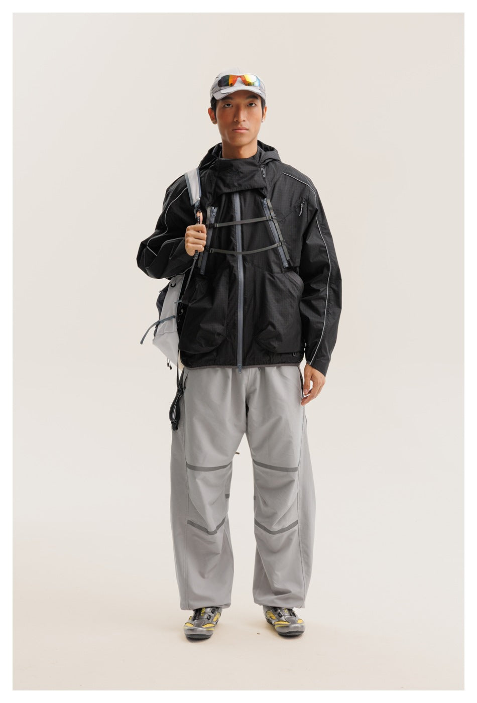 Front view of a model wearing a black hooded technical jacket and gray pants with reflective bands.