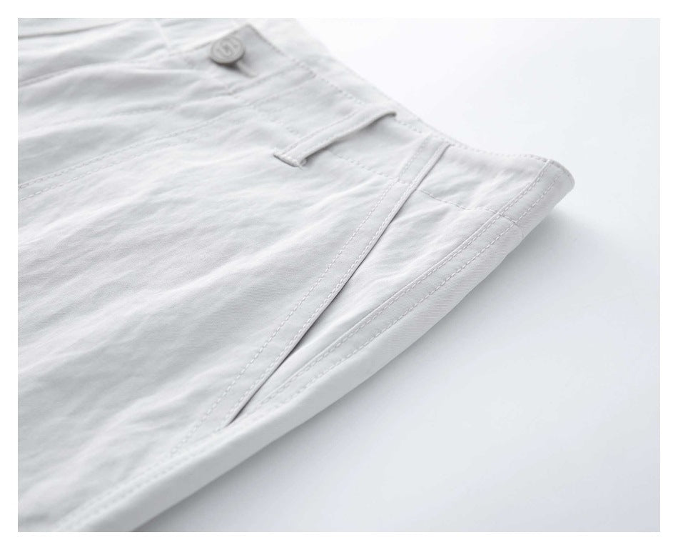 Close-up of white trousers showing a side pocket opening, waistband button, and stitched seams.