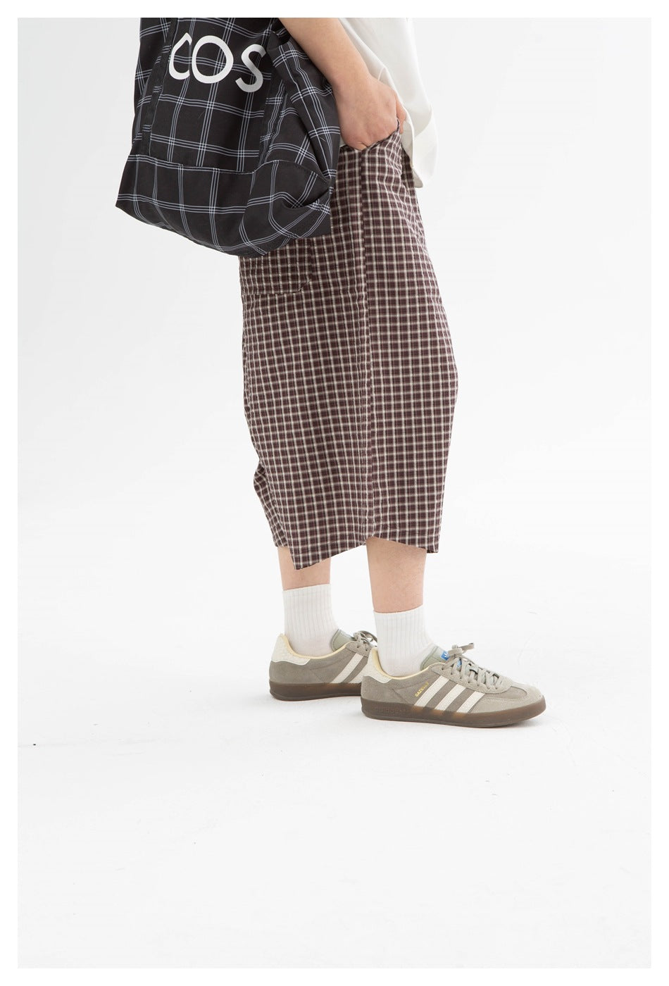 Side view of brown plaid knee-length shorts worn with a white shirt; a black checked tote is partly visible.