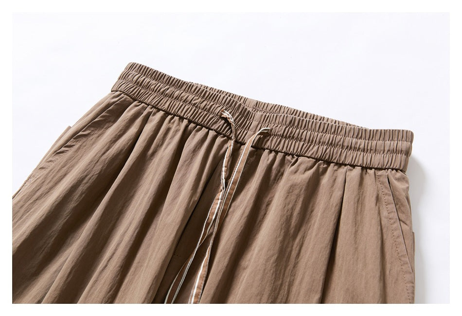 Close-up of taupe trousers with a gathered elastic waistband and long drawstring at the front.