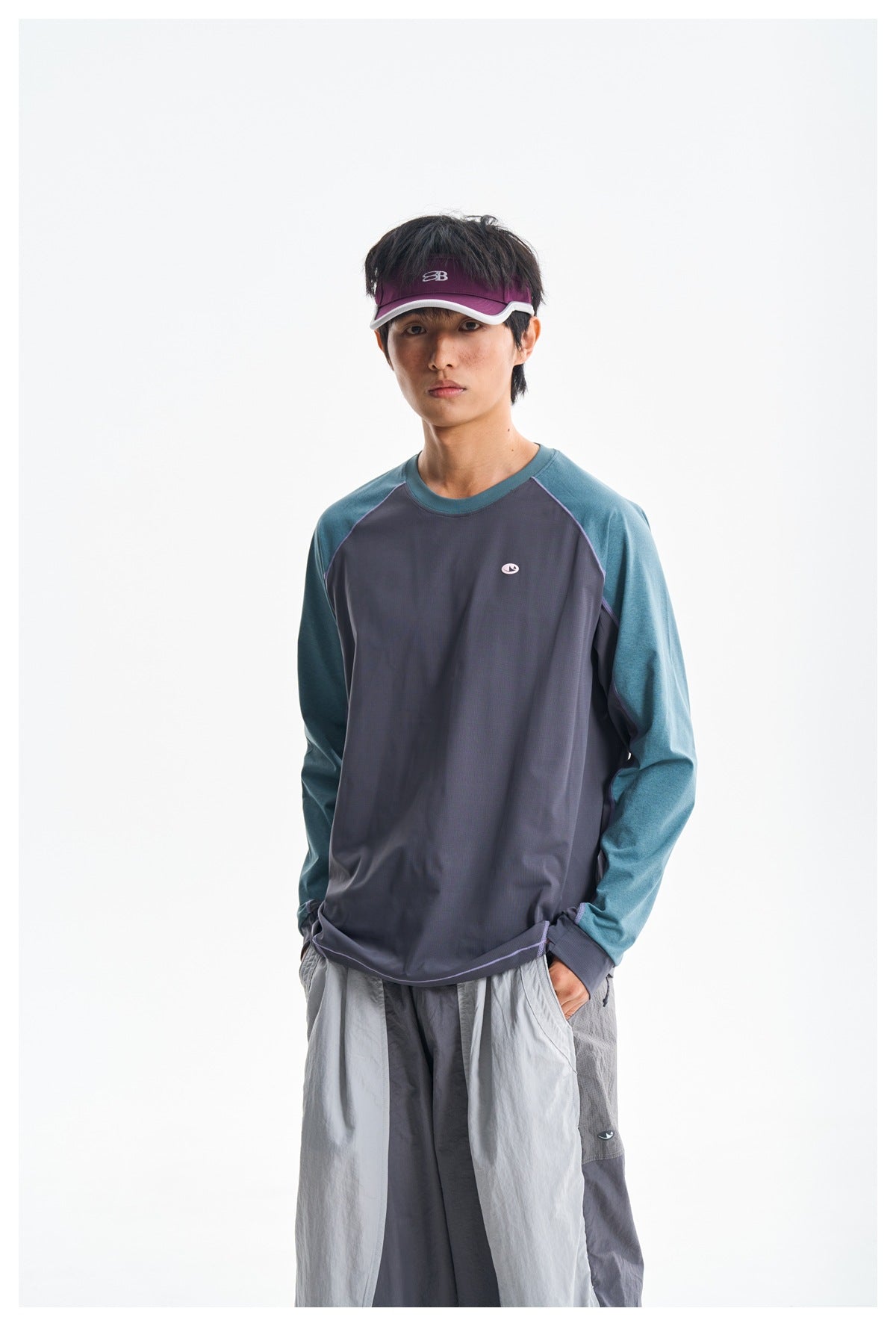 Model wearing a charcoal and teal color-block long-sleeve shirt with lavender piping and light gray trousers.
