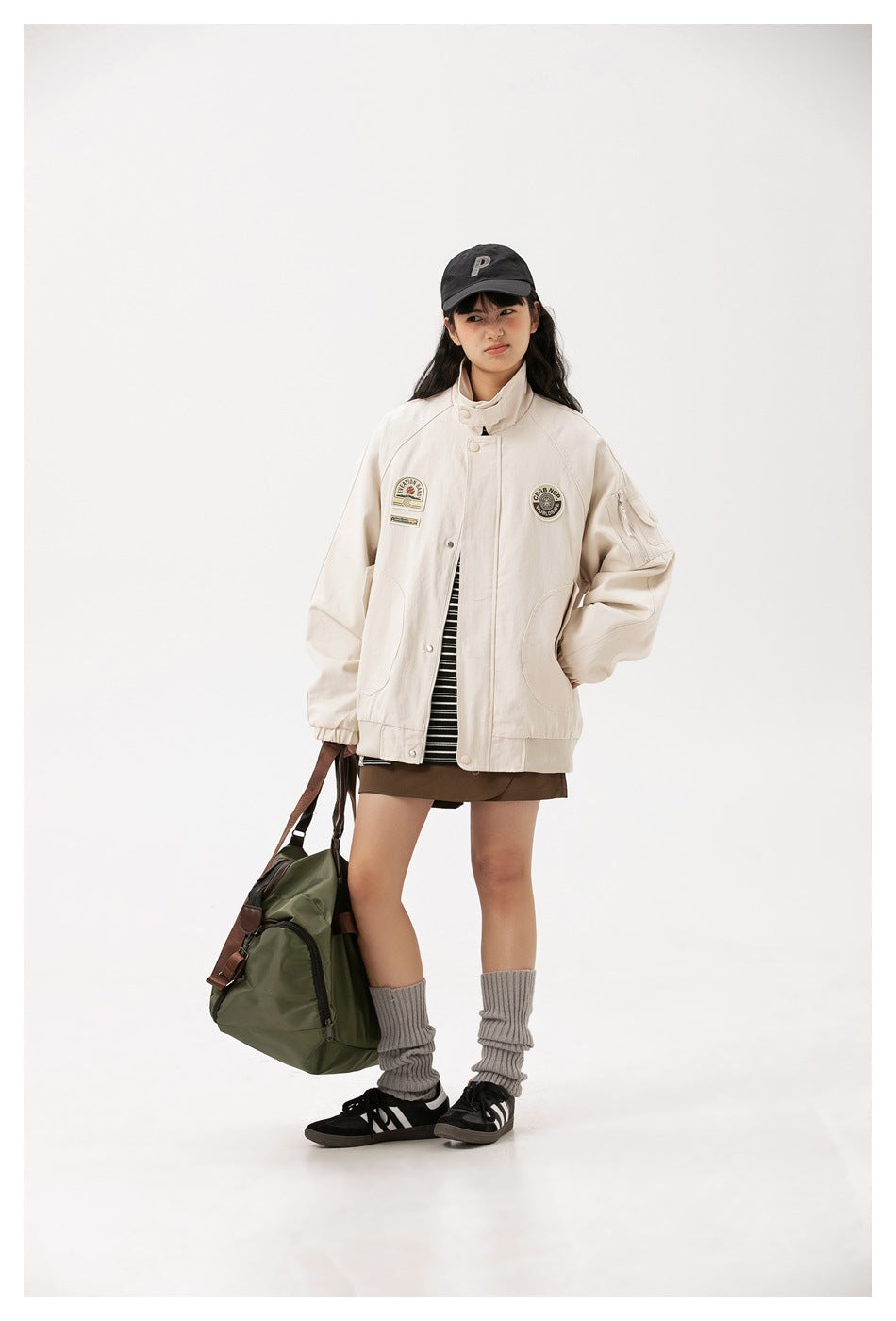 Model wears an ivory oversized jacket with patches, a high collar, and large pockets over a striped top.