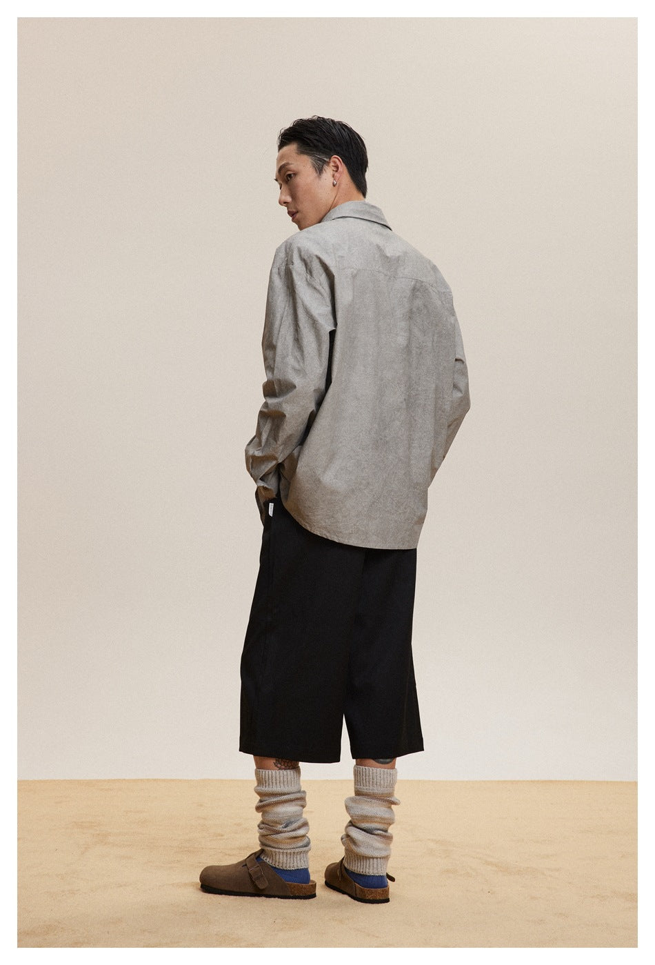 Back view of a model in a grey oversized shirt with black bottoms, knit leg warmers and clogs