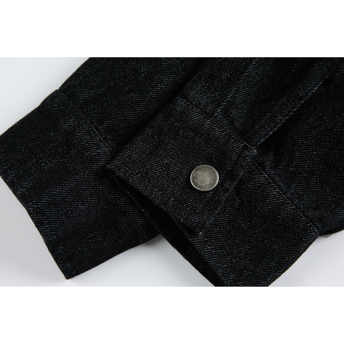 Close-up of a black jacket cuff with a round silver snap button.
