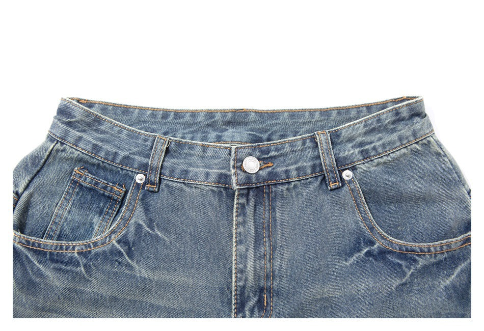 Front waistband close-up of blue washed denim pants, showing the button, belt loops, fly and curved pockets.