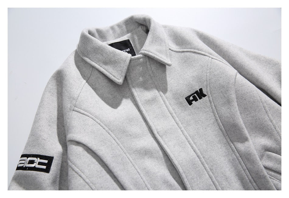 Close-up of the light gray jacket's collar, front seams, chest emblem, and black sleeve graphic.