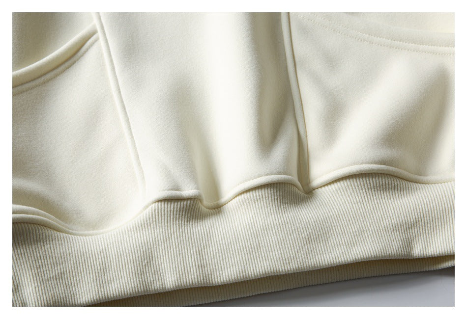 Close-up of an ivory hoodie’s lower front, pocket edge, and wide ribbed hem.