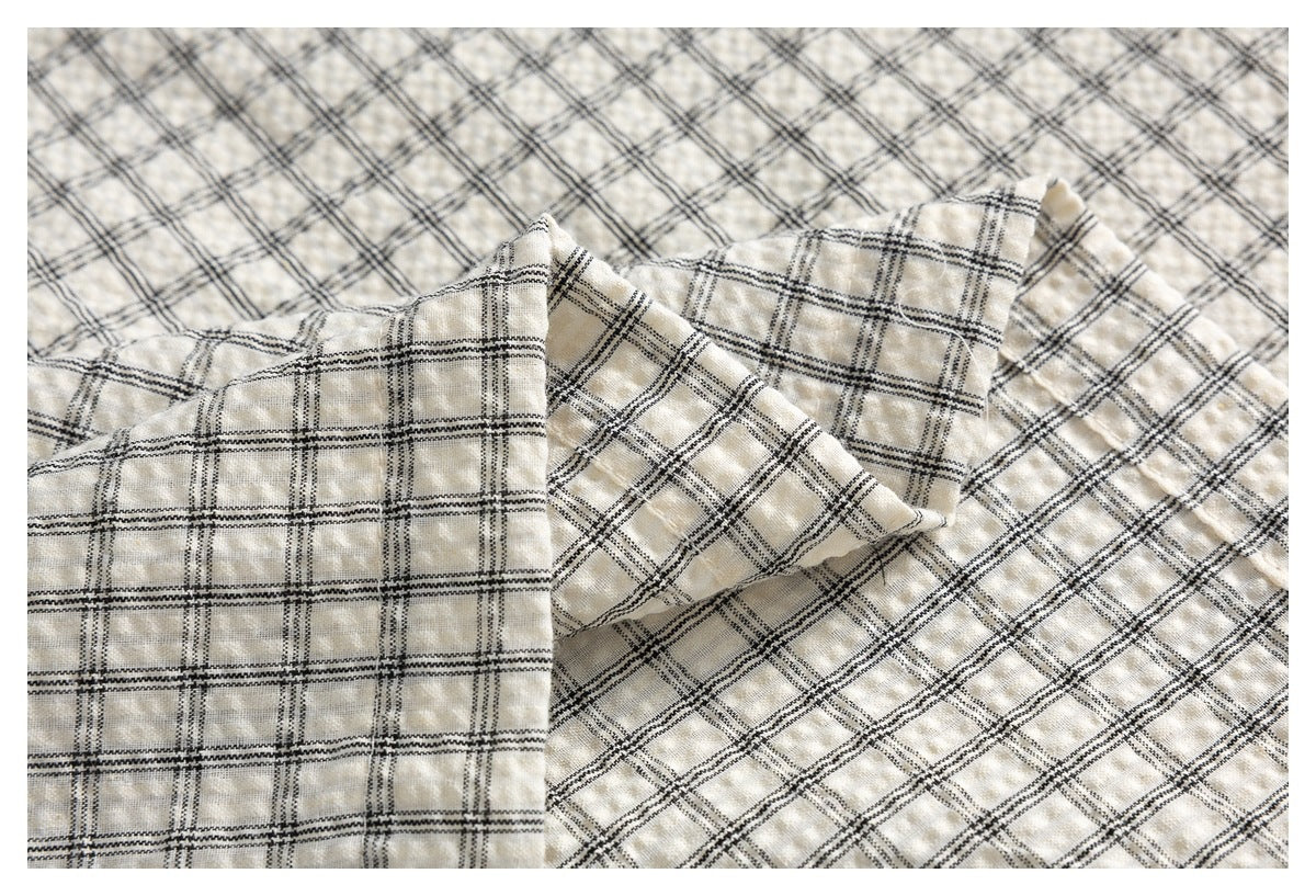 Close-up of folded cream fabric showing a black plaid pattern and softly textured surface.