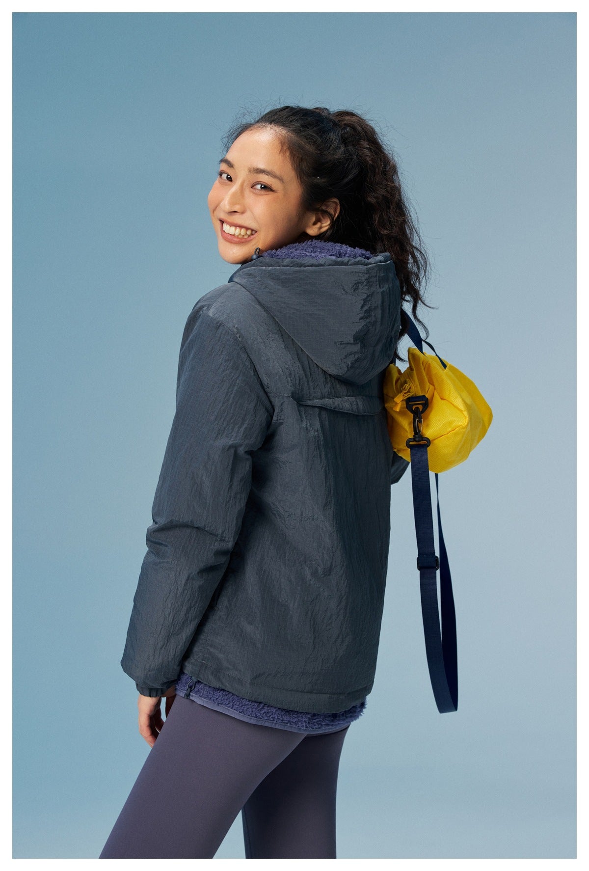 Back view of a woman wearing a dark slate hooded jacket with a yellow drawstring bag.