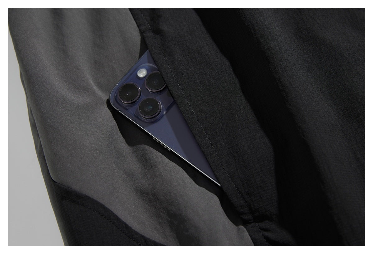 A smartphone tucked into a pocket on a black jacket, showing the pocket opening and stitching.