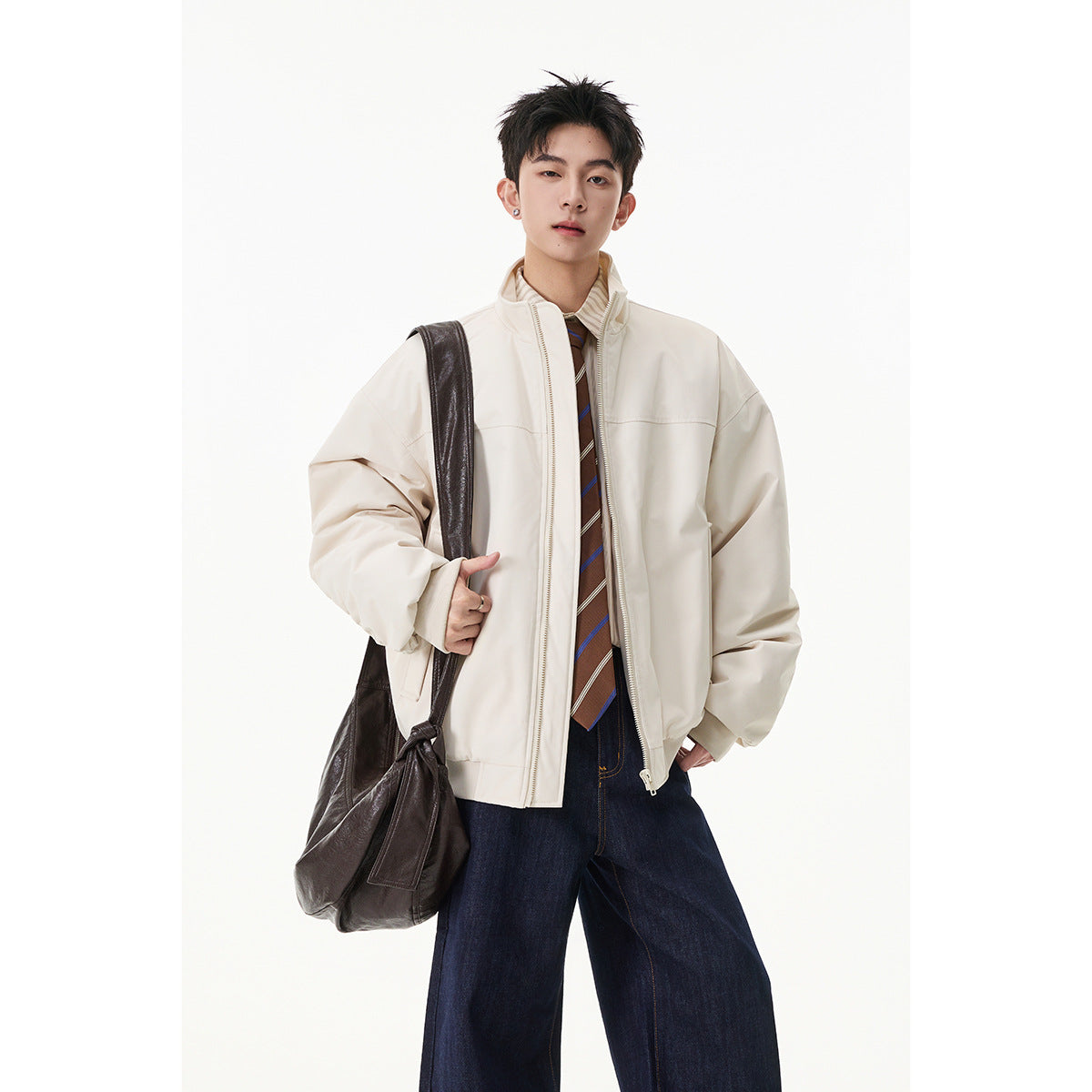 Model wearing an oversized ivory zip-up jacket with a stand collar, paired with wide dark jeans and a striped tie.