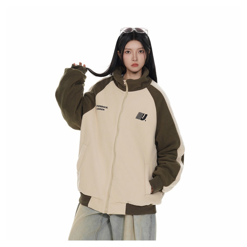 Closer view of a model in a cream and olive color-block zip-up jacket with a high collar and loose light-wash jeans.