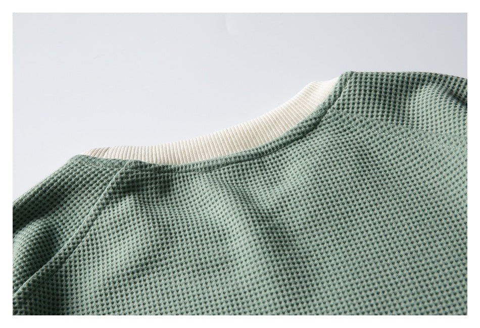 Close-up of a sage green textured knit garment with a cream ribbed neckline.