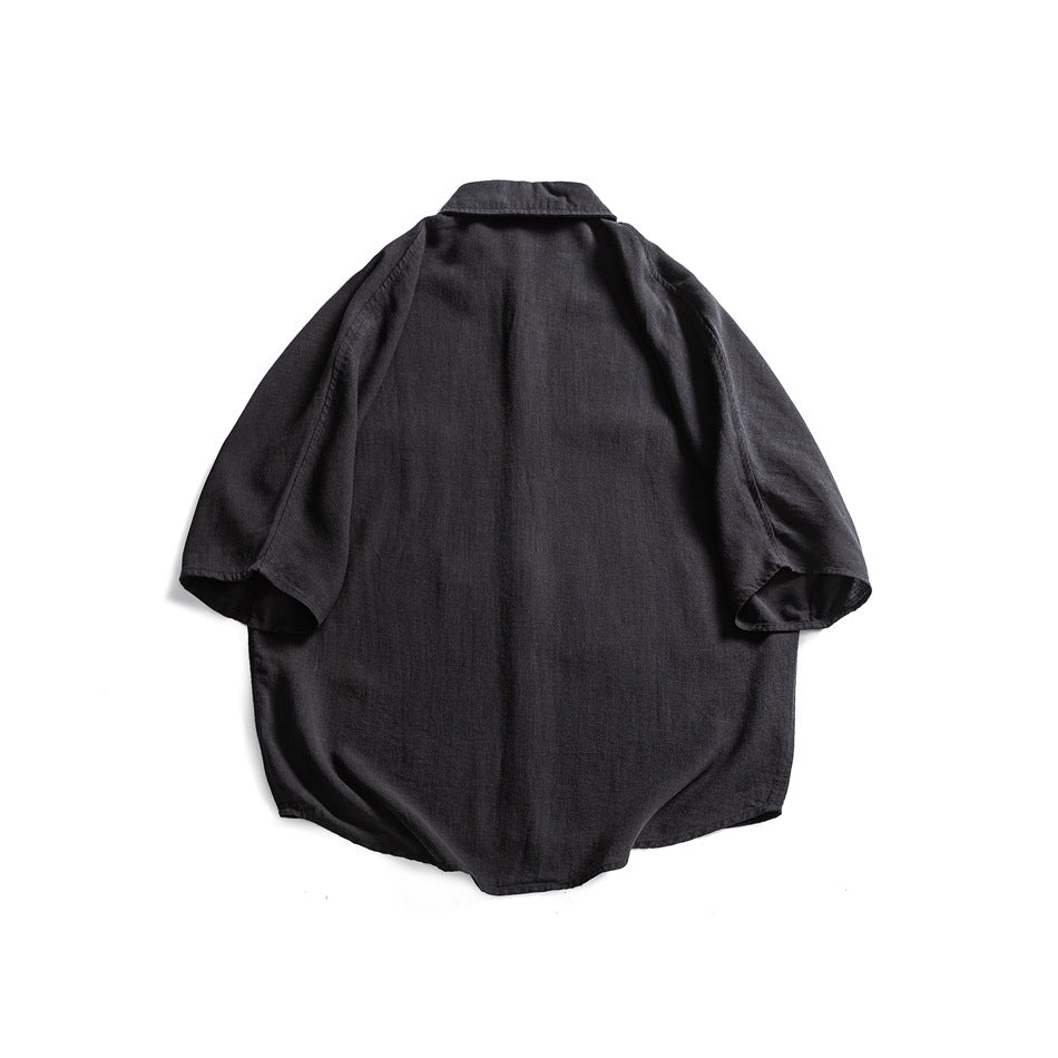 Back view of a black short-sleeve button-up shirt laid flat on white.