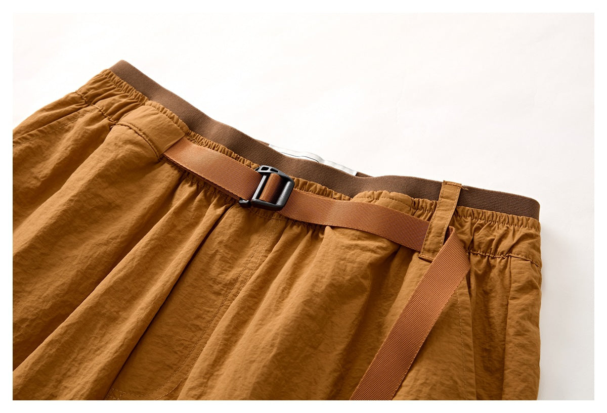 Close-up of rust-brown shorts showing the elastic waistband and adjustable webbing belt with a black buckle.