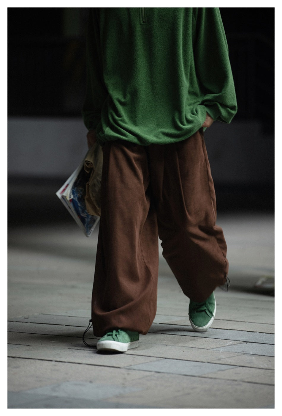 Cropped walking view of a person in a green pullover and loose brown pants with adjustable ankle cords.