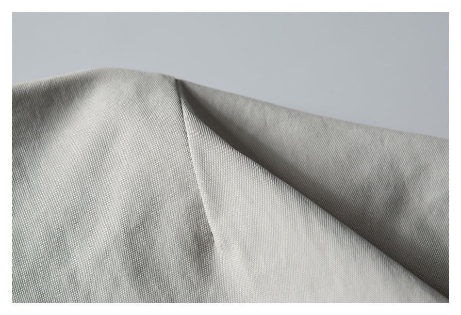 Close-up of light gray jacket fabric folded to show its fine surface texture.