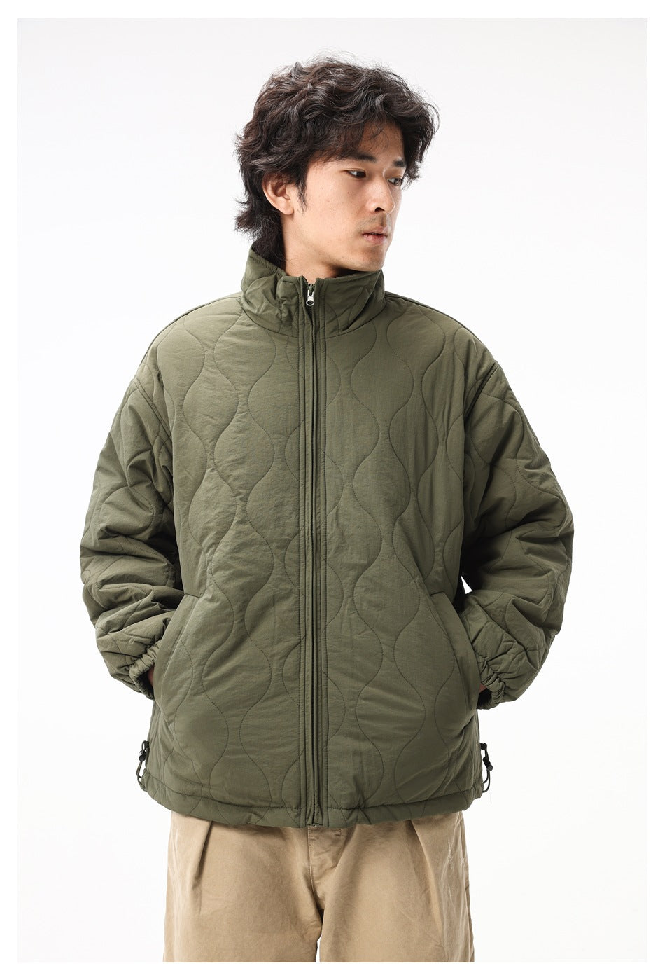 Front view of a man wearing an olive quilted jacket with a high collar, full-length zipper and side pockets.