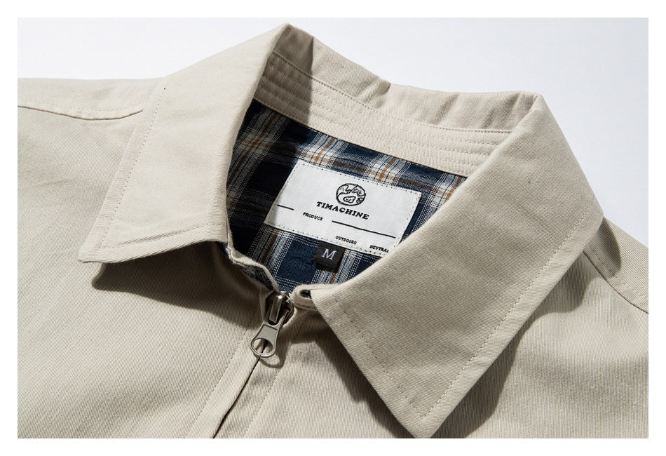Close-up of a beige jacket collar and zipper, showing blue plaid lining and a sewn neck label.