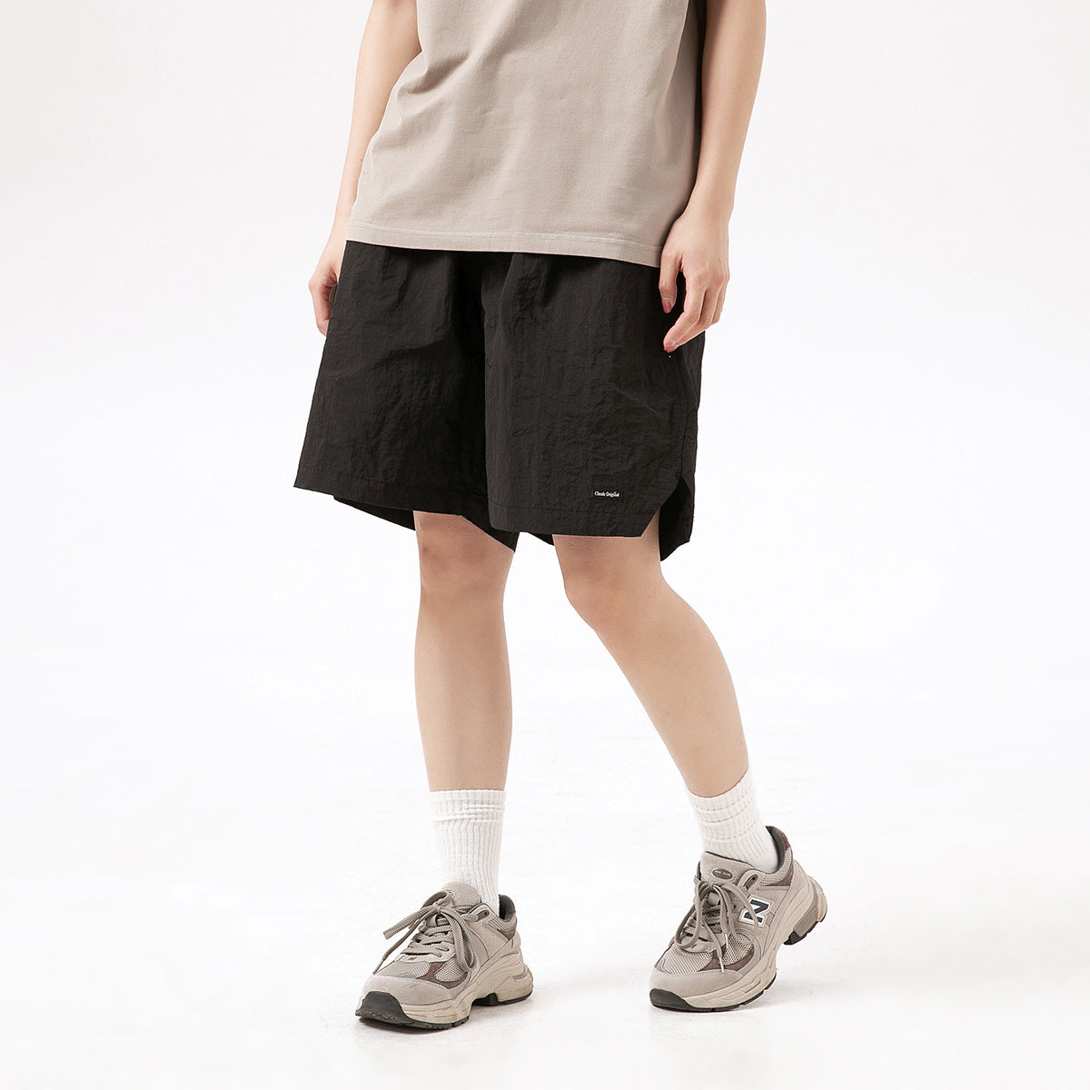 Cropped model wearing loose black shorts with a small hem label, a beige top, white socks, and gray sneakers.
