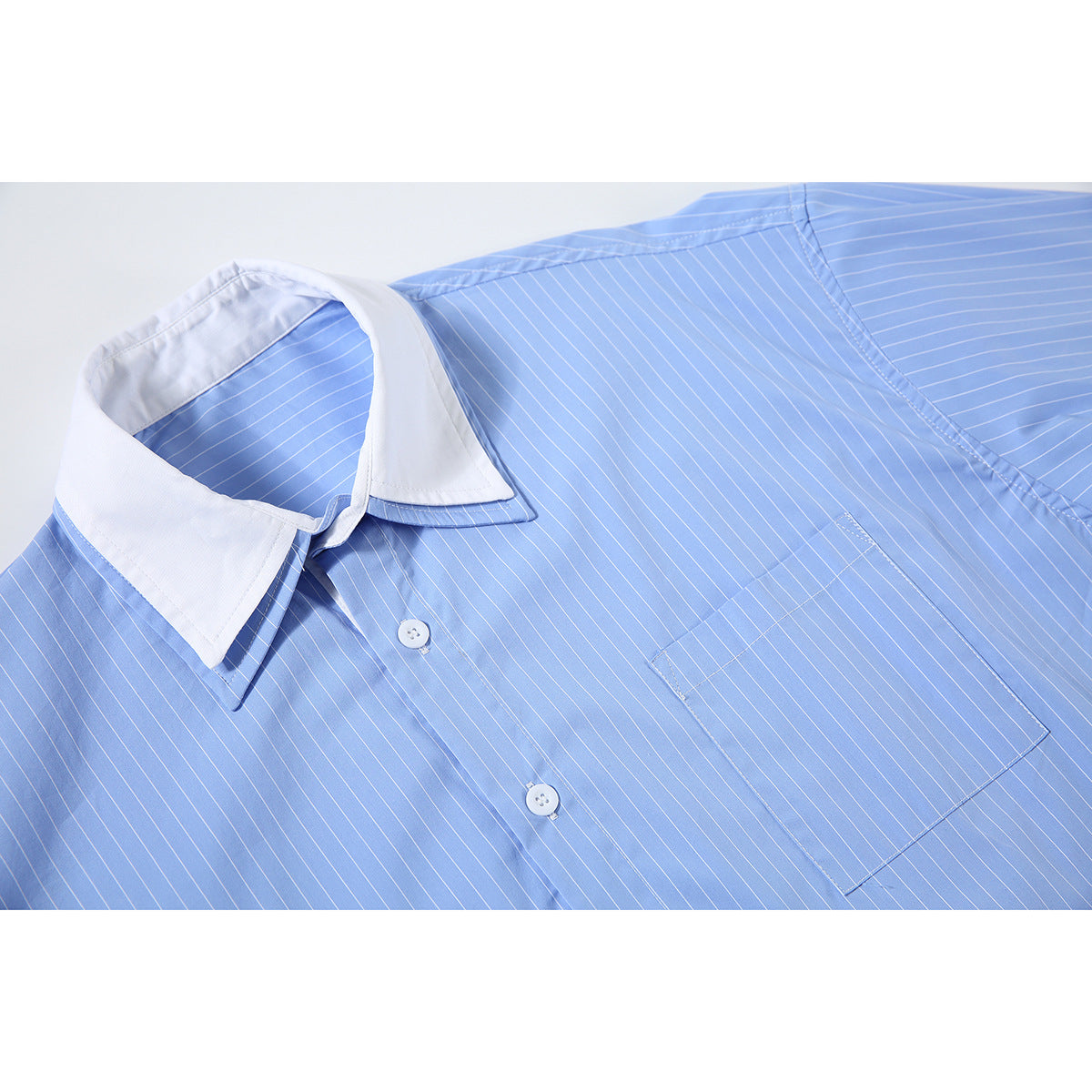 Close-up of a light blue pinstriped shirt with a contrasting white collar, buttons, and chest pocket.
