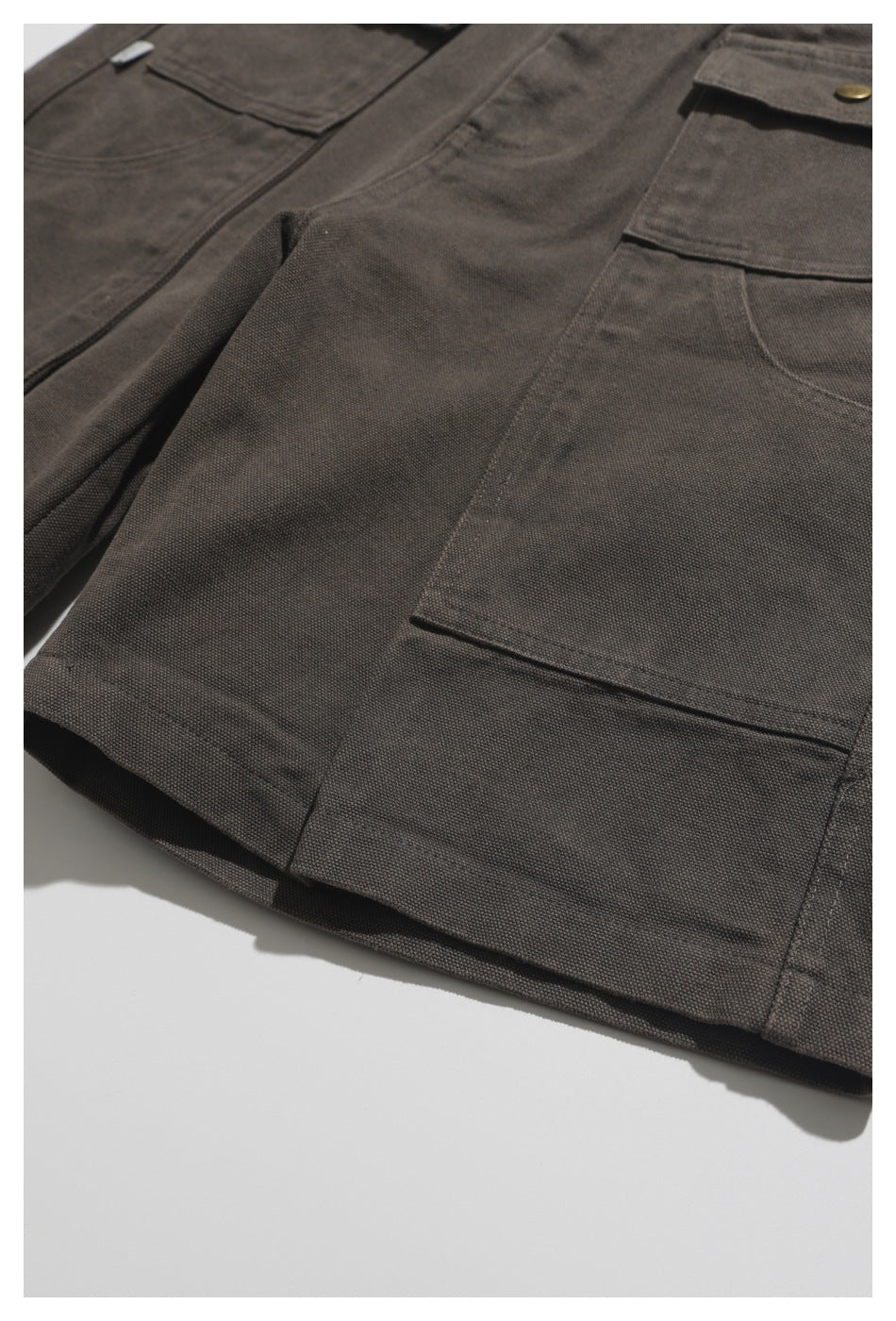 Close view of charcoal-brown utility trousers laid flat, showing large patch pockets and stitched seams.