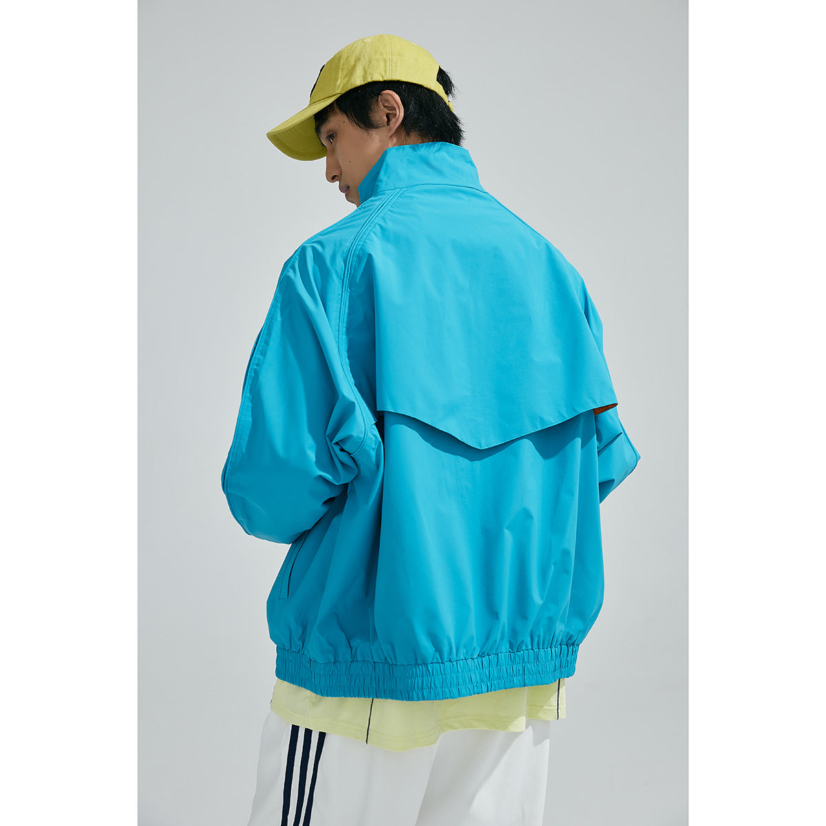 Model wearing the turquoise jacket, shown from behind with a layered back vent and elastic hem.