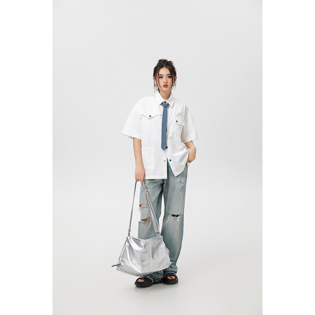 Model wearing an oversized white short-sleeve shirt with a blue tie and distressed jeans.