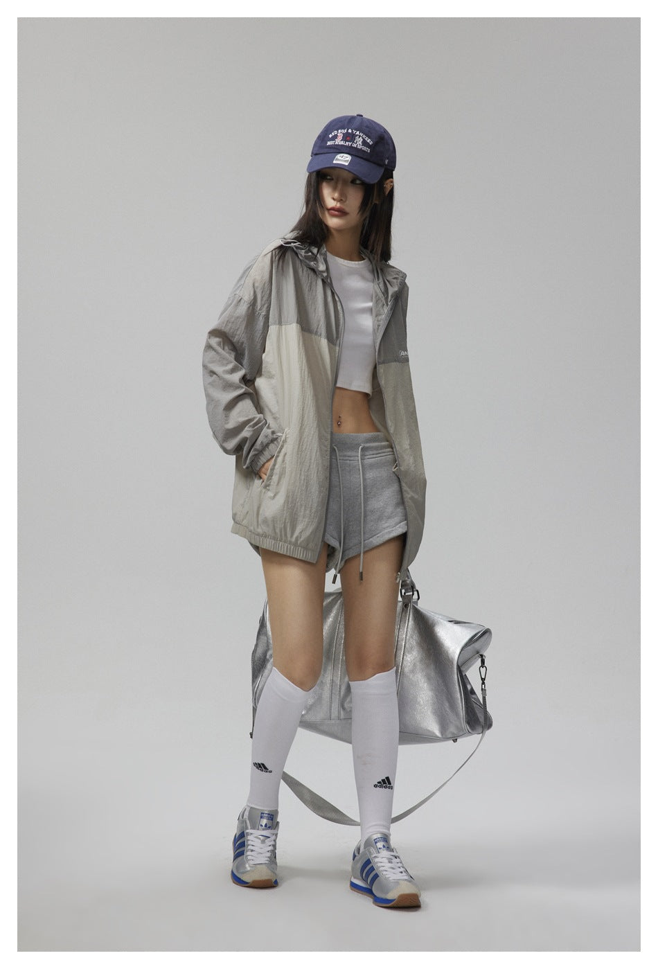 Model wearing an open gray and cream color-block hooded jacket with gray shorts and a navy cap.