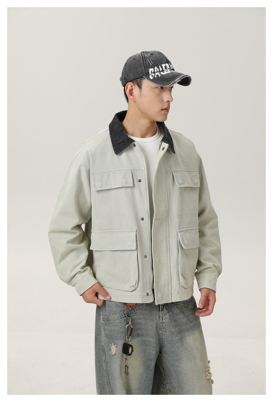 Closer front view of a model wearing a pale sage utility jacket with a black collar, zipper, buttons, and four flap pockets.