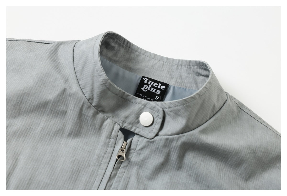 Close-up of a light gray jacket's stand collar, white snap, front zipper, and sewn neck label.