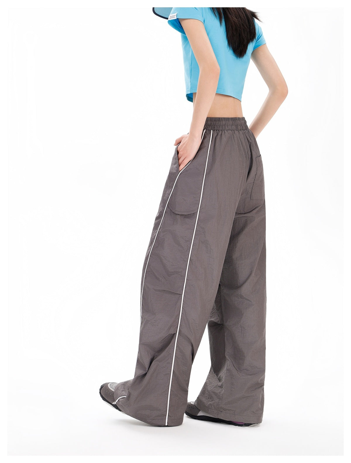 Side and rear view of a model wearing charcoal-gray wide-leg pants with white piping and a large side pocket.