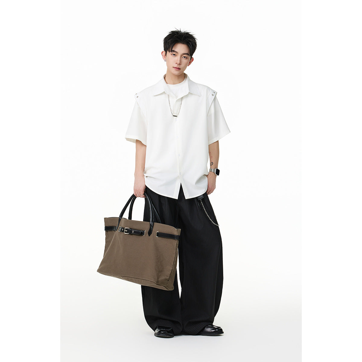 Model wearing a white short-sleeve button-up shirt and wide black pinstripe trousers, carrying a brown tote.