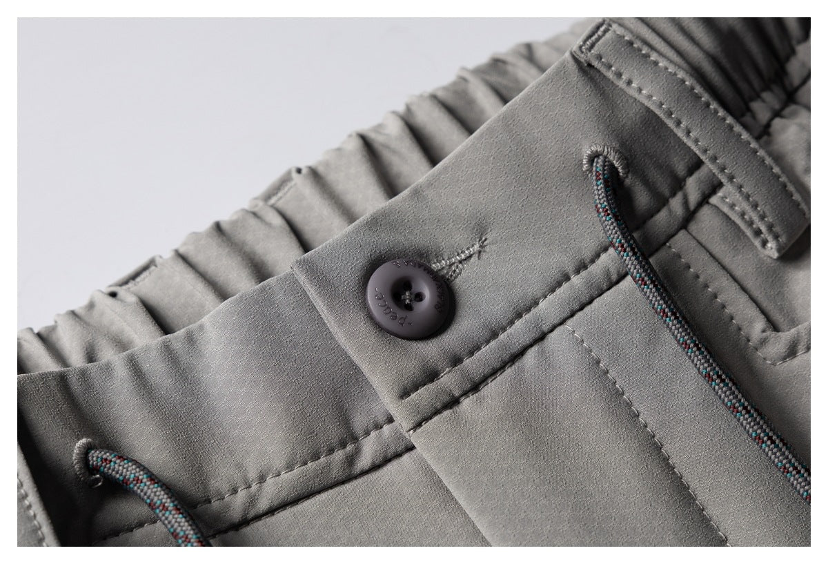 Close-up of gray shorts showing the waistband button, belt loop, stitching, and multicolored drawcords.