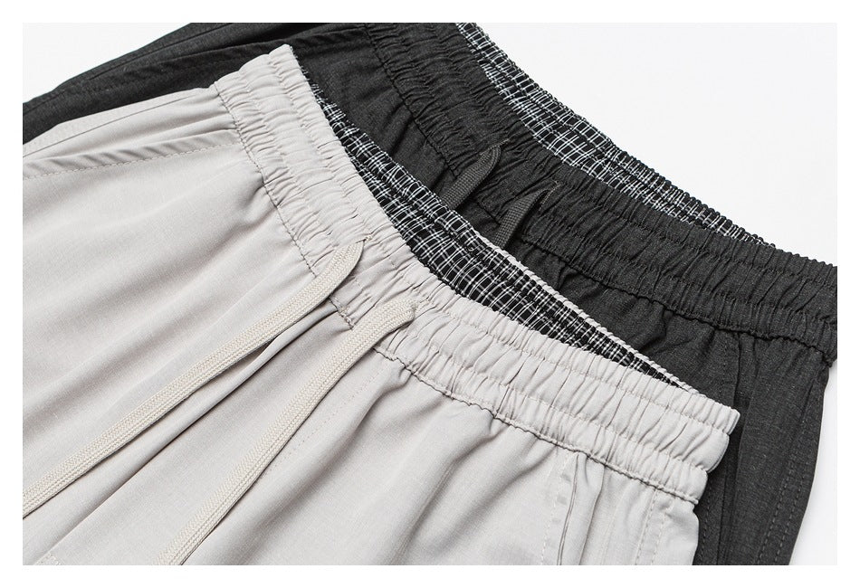 Close-up of layered elastic waistbands in light gray, black, and black-and-white plaid, with drawstrings on the gray pair.