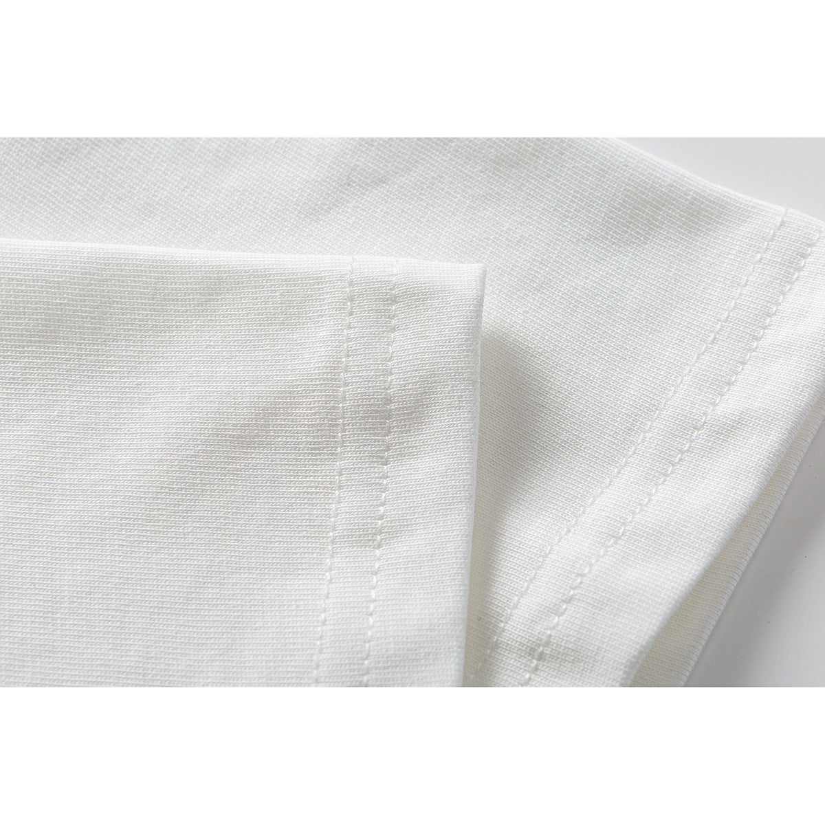 Close-up of white garment fabric showing a folded edge and parallel rows of stitching.