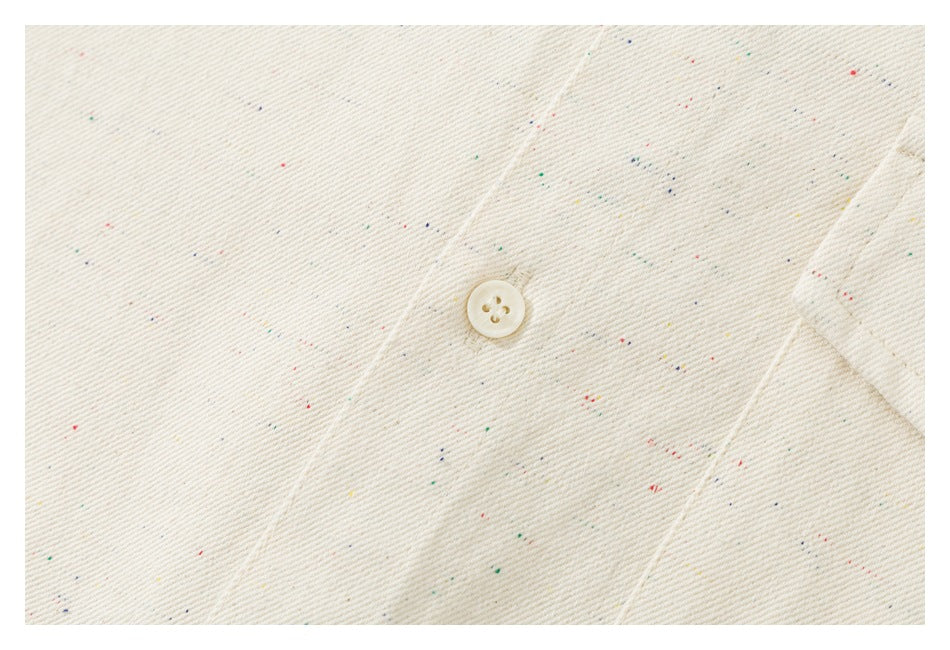 Close-up of an ivory shirt’s textured, multicolored-flecked fabric and a cream button.
