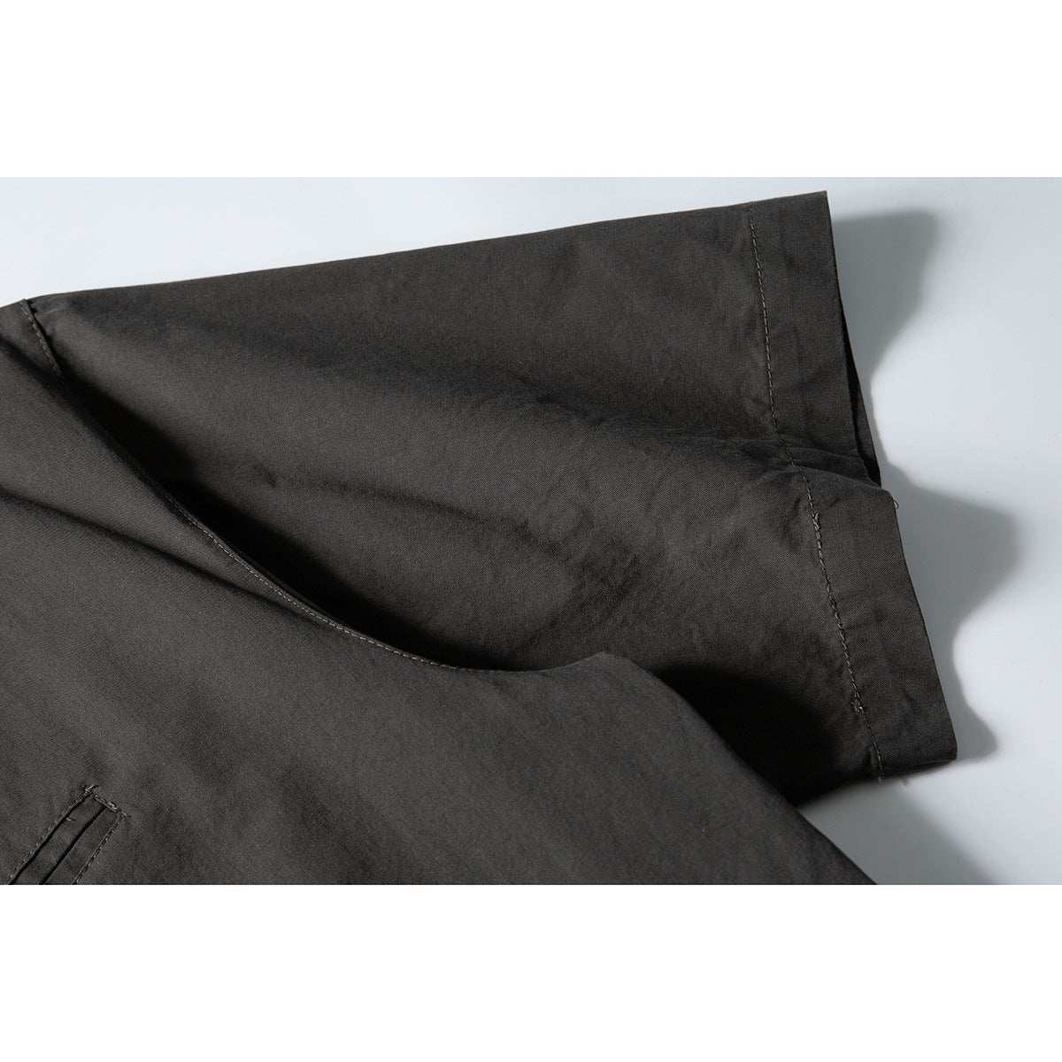 Close-up of a charcoal garment showing a folded edge, stitching, and part of a pocket.