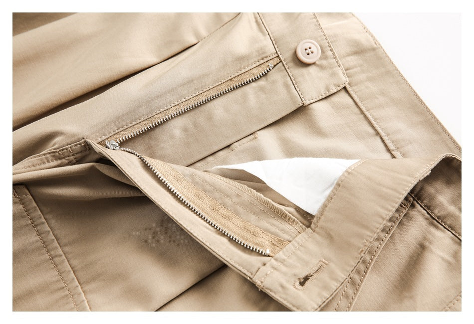 Close-up of beige trousers showing the waistband button and an open zipper fly.