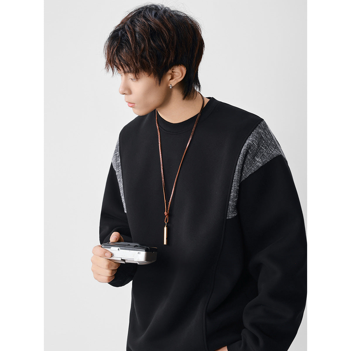 Side-view model wearing a black crewneck sweatshirt with contrasting textured gray shoulder panels.