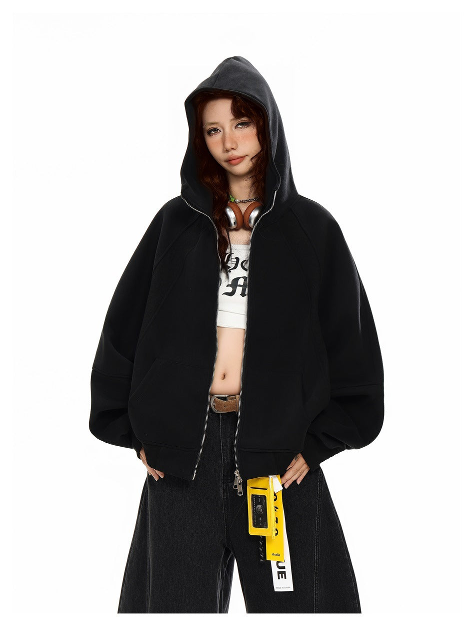 Model wearing a black oversized zip hoodie with the hood up, open over a white graphic crop top.