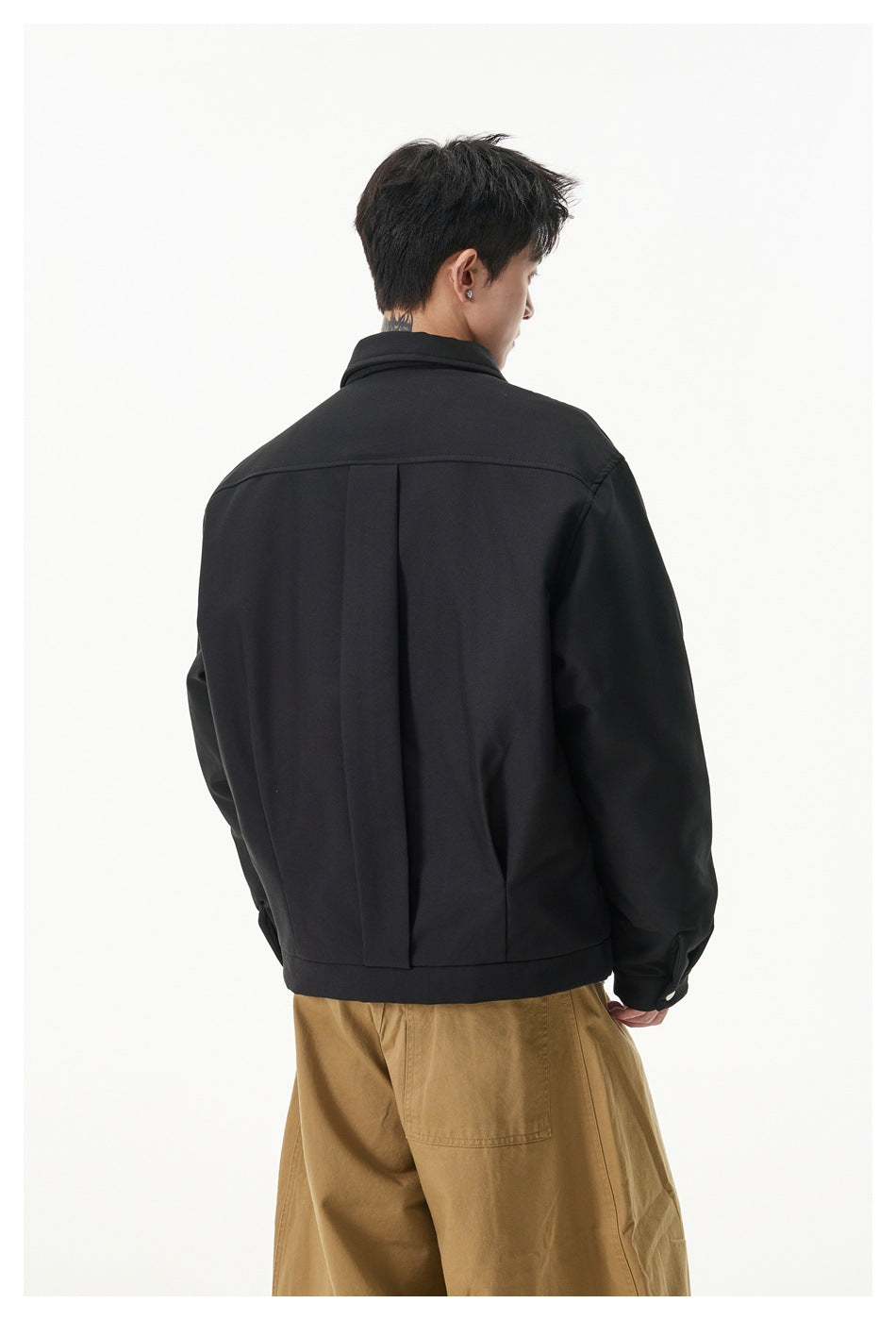 Back view of model in black collared jacket showing center back pleat, with tan pants