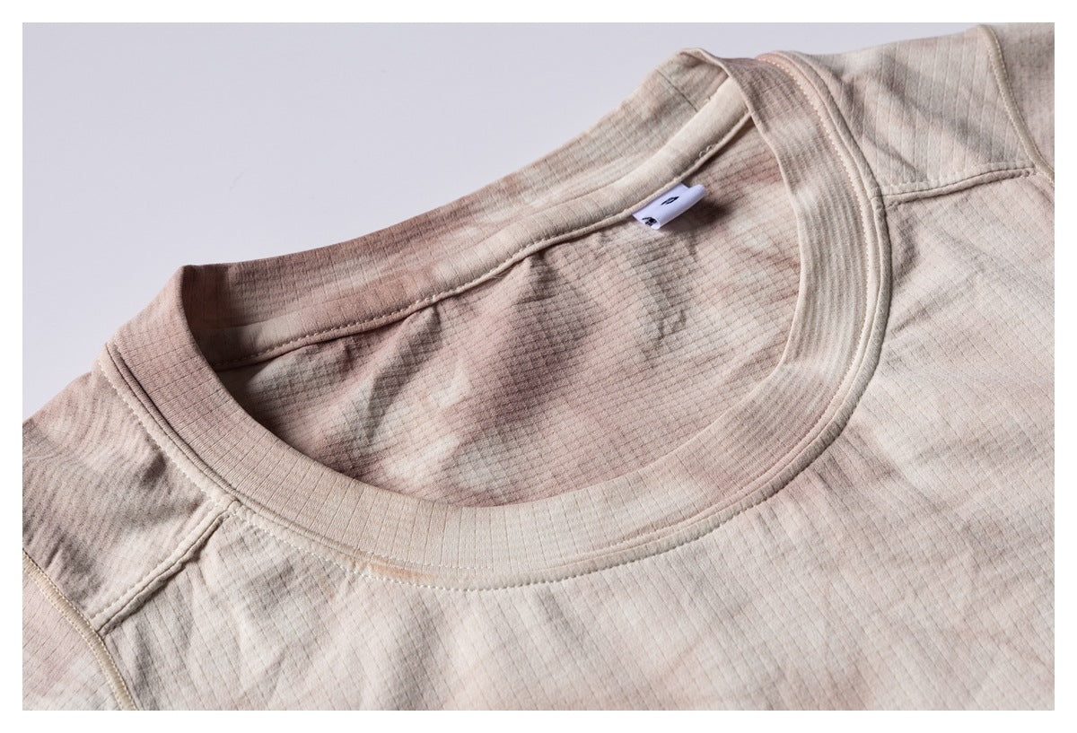 Close-up of a beige crew-neck shirt showing its ribbed collar, inner label, and muted brown mottled pattern.