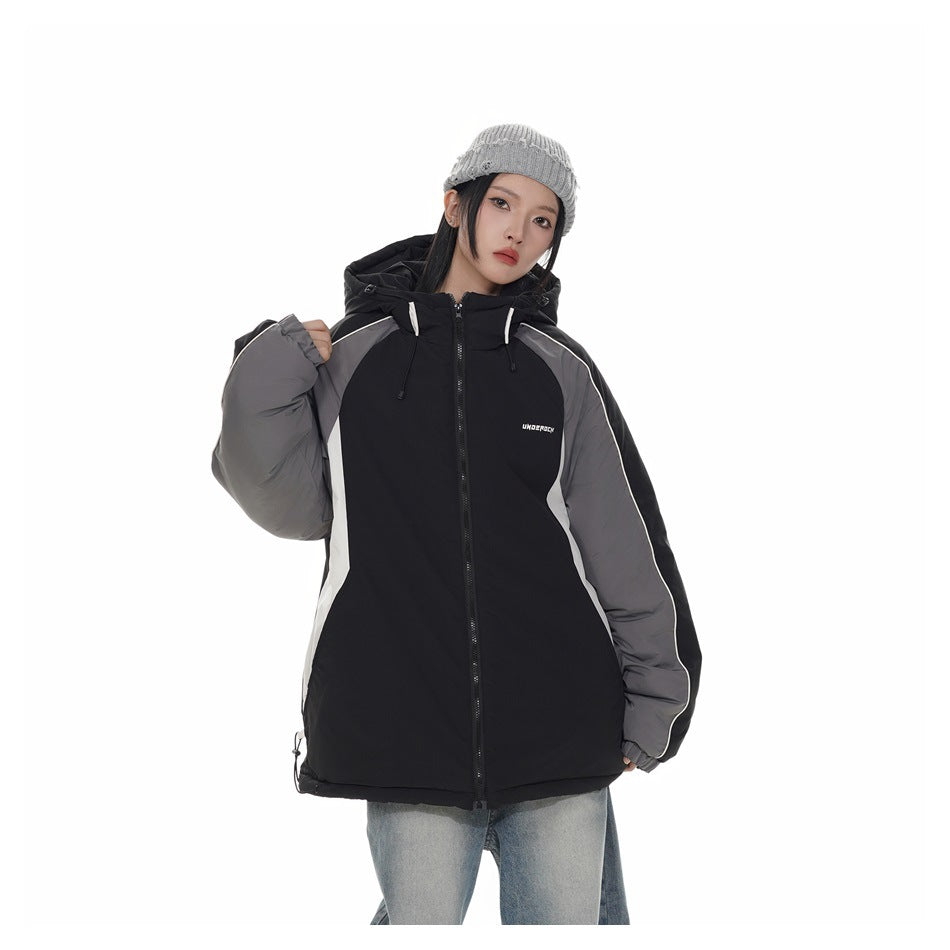 Model wearing a black zip-up hooded jacket with gray sleeves and white piping, with a gray beanie and light jeans