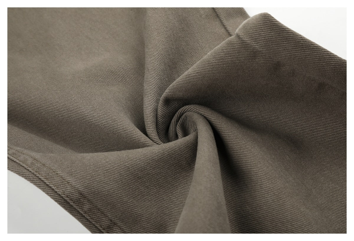 Close-up of taupe-gray twill trousers fabric gathered into soft folds, showing its diagonal weave and stitching.