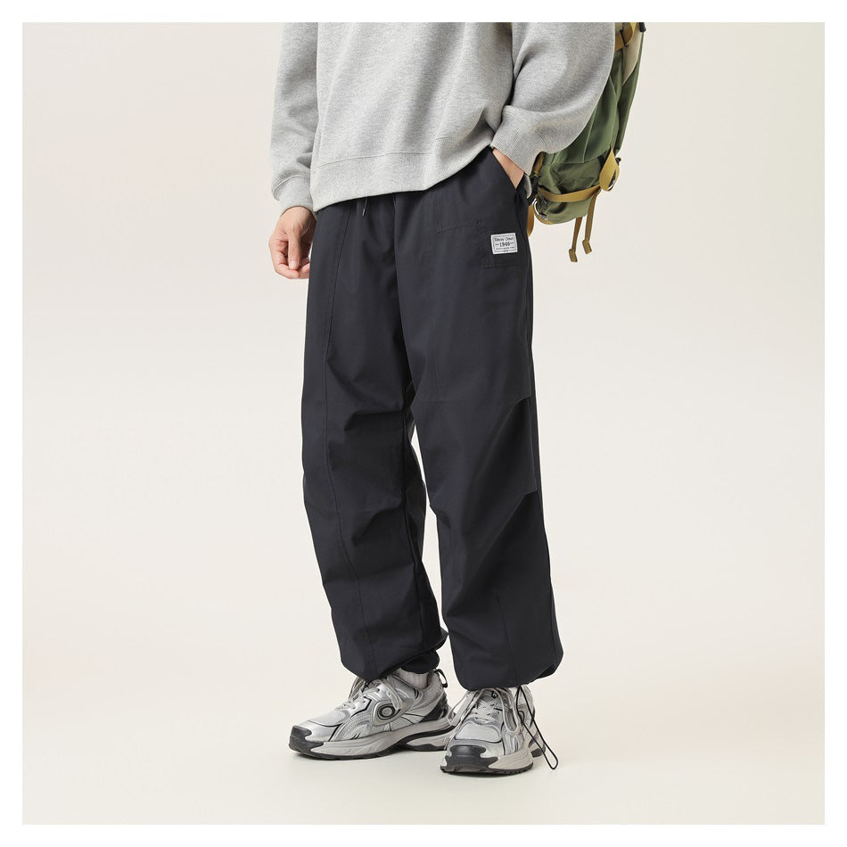 Front view of a model wearing loose black pants with a small thigh label, gray sweatshirt, and sneakers.