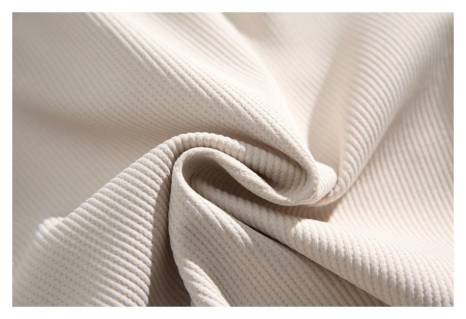 Macro view of soft-looking cream fabric with pronounced vertical ribbing, folded into a spiral.